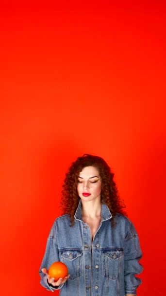 Young curly girl throws orange on a coral background in the studio — Stock Video