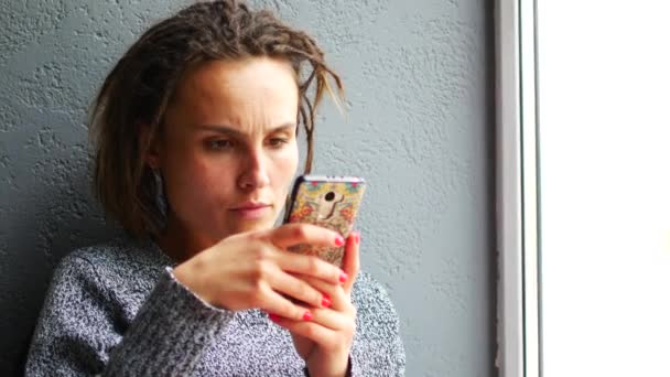 Fiatal kaukázusi lány élvezi a mobil okostelefon egy kávézó ablak. — Stock videók