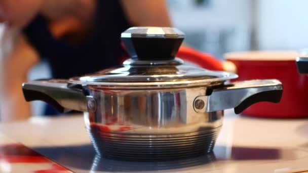 Sartén en la estufa en la cocina, la señora se queja en el fondo — Vídeo de stock