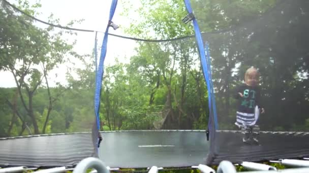 Girl jumping on a trampoline that stands in the park among the trees — Stock Video