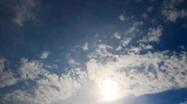 Mavi gökyüzüne karşı yüzen bulutların zaman atlamalı. Bulutların arasından güneş