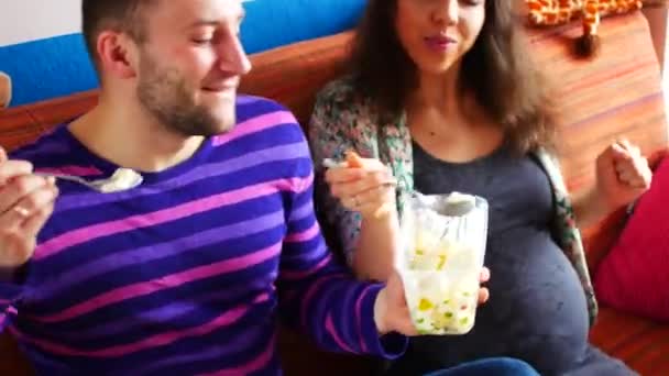 Молода пара годує один одного морозивом, сидячи на дивані — стокове відео