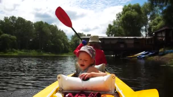 Een kind in een kajak op de rivier. Gezinsactiviteiten buiten. — Stockvideo