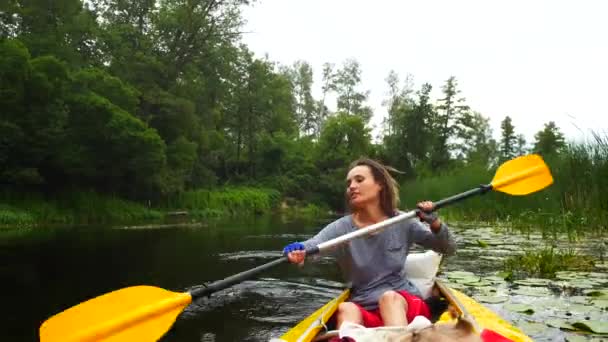 Uma jovem trabalha duro com uma raquete em um caiaque no rio — Vídeo de Stock