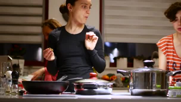 Kobieta gospodyni przygotowuje jedzenie w kuchni w towarzystwie jej przyjaciół. — Wideo stockowe