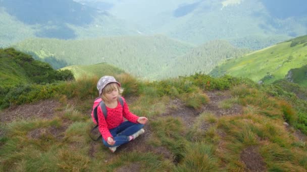 Un niño medita en una posición de loto en la cima de una montaña . — Vídeo de stock