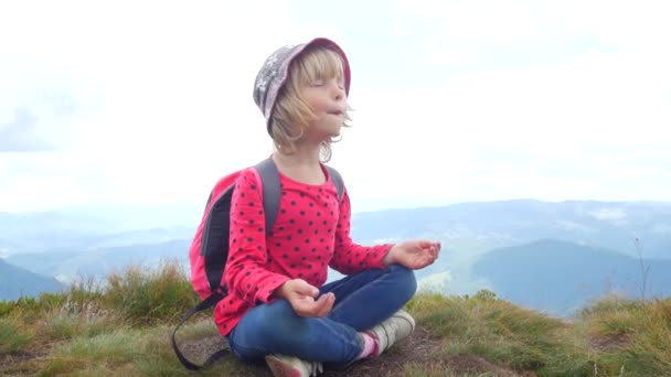 Un niño medita en una posición de loto en la cima de una montaña . — Vídeos de Stock