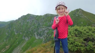 Dağın tepesinde ki çocuk kız. Kaya parmaklarını gösterir.