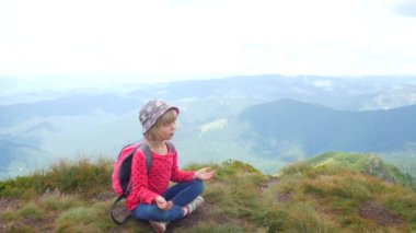 Bir çocuk bir dağın tepesinde lotus pozisyonunda meditasyon yapar..