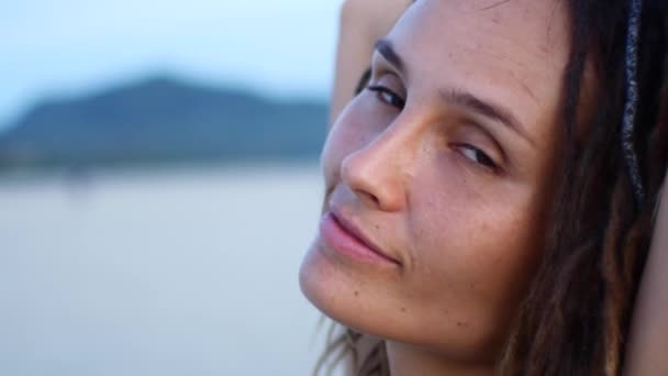 Een vrouw met dreadlocks kijkt naar de camera en glimlacht. Strand — Stockvideo