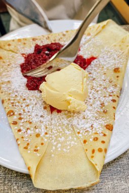 Vanilyalı dondurma, ahududu sosu ve beyaz tabakta servis edilen pudra şekerli krep.