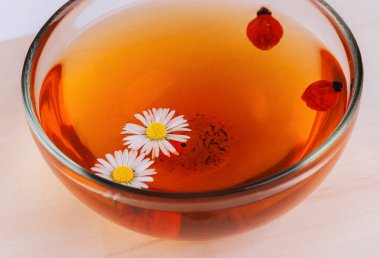 Bir bardak vitamin zengini, papatya çiçekli ve gül kalçalı bitki çayı.