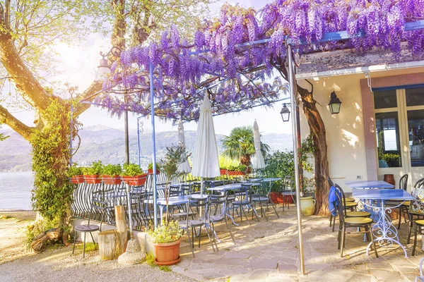 Terrace of outdoor small retro cafe decorated with flowers of wisteria on the Italian coast in a sunny spring evening. Lake Lago Maggiore in Stresa, Italy