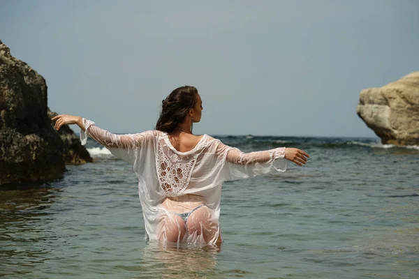 妇女在湿衬衣与举起的手站立在海后方看法 — 图库照片