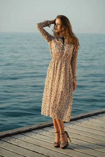 妇女在夏天礼服站立在木码头由日落 — 图库照片