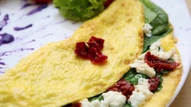 Bırakır dryed domates, Yunan beyaz peynir, taze yeşil ıspanak ile lezzetli omlet yemek brunch için kafede beyaz tabakta servis edilir. Restoran lezzetli doğal gıda öğle yemeği için. Omlet sabah tadını çıkarın.