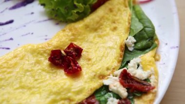 Bırakır dryed domates, Yunan beyaz peynir, taze yeşil ıspanak ile lezzetli omlet yemek brunch için kafede beyaz tabakta servis edilir. Restoran lezzetli doğal gıda öğle yemeği için. Omlet sabah tadını çıkarın.