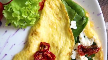 Bırakır dryed domates, Yunan beyaz peynir, taze yeşil ıspanak ile lezzetli omlet yemek brunch için kafede beyaz tabakta servis edilir. Restoran lezzetli doğal gıda öğle yemeği için. Omlet sabah tadını çıkarın.