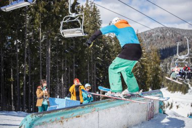 BUKOVEL,UKRAINE-24 MARCH,2018: Extreme skiing jib contest in snow park.Ski rider grinds on rail with freeskis in sunny winter day.Young athlete performs stunt on short skis clipart