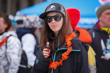 Bukovel, Ukrayna-19 Mart, 2018: Genç ve güzel esmer binici kız Jagermeister alkol içki bardak elinde tutar. Kış eylem Festivali kar Park spor. Aktif gençlik yaşam tarzı.