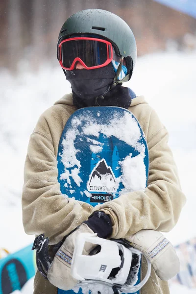 保護用のヘルメット 雪のボードを保持しているサングラスを身に着けているティーンエイ ジャー仮面ライダー男の子のブコヴェリ ウクライナ 2018 Portrat 冬のアクション スポーツ 雪の公園でお祭りです 若い人々 — ストック写真
