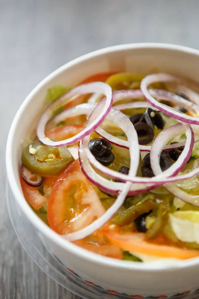 Top view greek salad with fresh vegetables served in paper plate in fast food restaurant menu.Overhead close up shot.Red onion rings,sliced tomato,pepper & black olives with olive oil