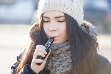 Soğuk kış günü içinde genç kız vaping dışında. Esmer kız vape ecig ejuice ile gülümseyen. Sigarayı ve sağlığını geliştirmek için Modern e-sıvı vaper aygıtı. Popüler elektronik aygıtı 