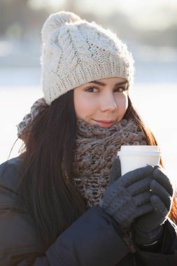 Güzel genç beyaz esmer kadın tutun ısınma sıcak cappuccion ya da kafeinsiz kahve fincanı soğuk parlak kış günü açık. Çok kadın model dışında sıcak kış giysilerle poz 