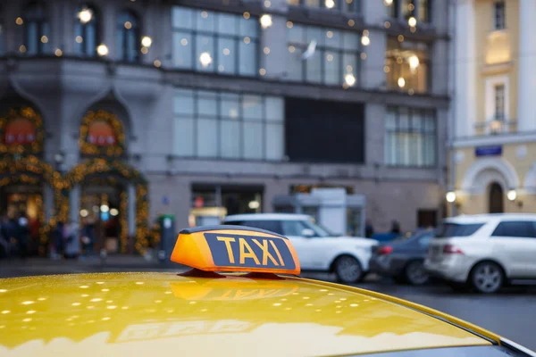 Yellow taxi car with orange icon on roof parked in city street waiting for passengers to pick up on city streets background.Focus on yellow lantern sign