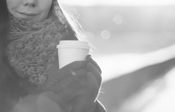 Pretty young woman drinks hot latte coffee drink from white paper takeaway mug.Brightly backlit scene,bright winter day.Frozen white girl get warm with cappuccino cup.Place logo and text on cup