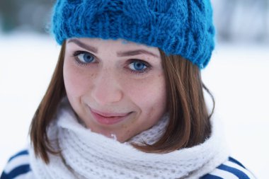 Funny young ginger girl making faces.Blurred background.Beautiful young white girl in warm blue knit winter hat posing outdoor.Winter blurry background out of focus.Place text over blur backdrop 
