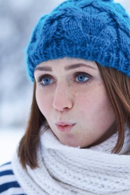 Funny young ginger girl making faces.Blurred background.Beautiful young white girl in warm blue knit winter hat posing outdoor.Winter blurry background out of focus.Place text over blur backdrop 