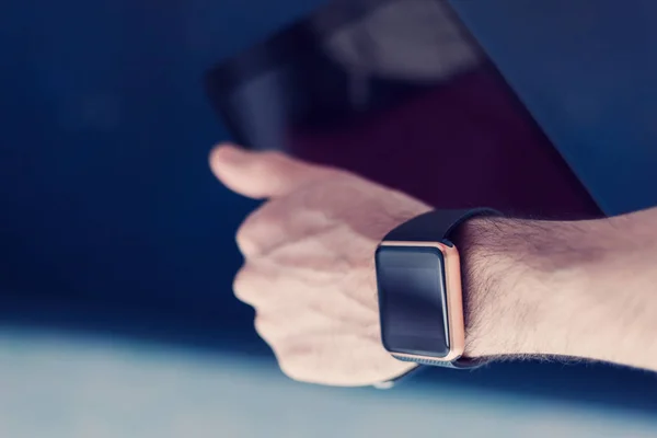 Male hand with two devices on it - trandy smart watch and tablet pc. This person is always connected to internet and social media with modern gadgets. Blue hipster film toning