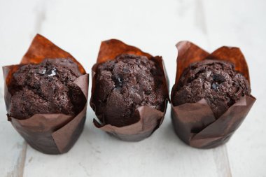 Kafede lezzetli çikolatalı kekler. Beyaz ahşap masa üzerinde dekoratif kağıt üç taze çikolatalı kek. Metni yerleştirmek için alanı kopyalama,odağı kapatma. 