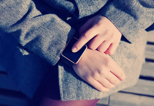 Female using her trendy smart wrist watch. This person is always connected to social media and internet. Modern technology and vintage hipster film toning