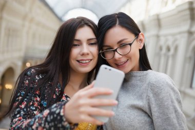 Selfie büyük modern gümüş akıllı cep telefonu ile alışveriş merkezinde alarak iki çekici genç kadın. Mutlu beyaz kızlar, yeni smartphone aygıtı