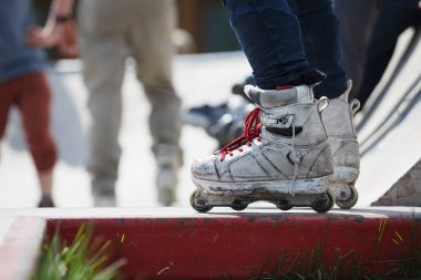 Açık skate Park beton bir rampa üzerinde oturan agresif inline paten giymiş patenci ayakları. Silindir bıçakları için hile ve biler giyen aşırı spor atlet 