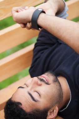 Bir parkta bankta oturan trendy akıllı saatini kullanan genç siyah adam. Internet, şamata sosyal medya her zaman kalmak sağlar bağlı Modern gadget. 