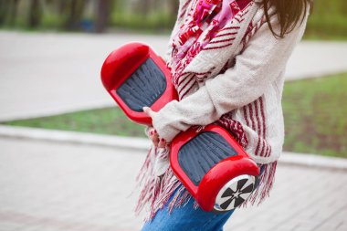 Kadın modeli modern kırmızı elektrikli mini segway ya da vurgulu kurulu scooter parkta yürürken elinde tutan. Hava kirliliği atmosfere üreten popüler yeni ulaşım teknolojisi. Kız gidişli boho tarzı kıyafetler giyiyor. 