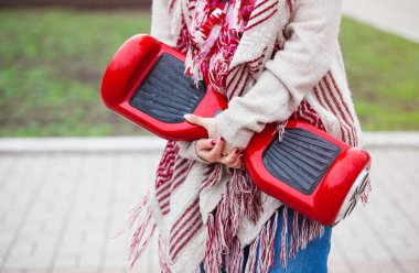 Kadın modeli modern kırmızı elektrikli mini segway ya da vurgulu kurulu scooter parkta yürürken elinde tutan. Hava kirliliği atmosfere üreten popüler yeni ulaşım teknolojisi. Kız gidişli boho tarzı kıyafetler giyiyor. 