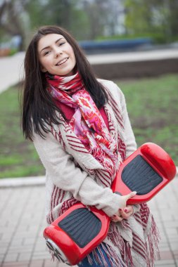 Esmer beyaz girll modern kırmızı elektrikli mini segway ya da vurgulu kurulu scooter parkta yürürken elinde tutan. Popüler yeni becerikli alet. Kız trendy boho tarzı kıyafetler giyiyor. 
