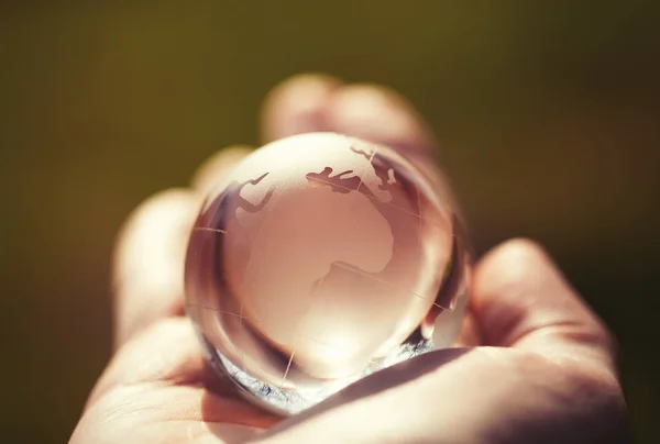 Man holding crystal glass globe model in his hand. Macro photo, shallow depth of field. Concept for care, international affairs, global business