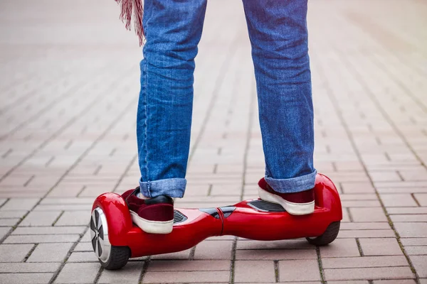 Feet of a girl riding on modern red electric mini segway or hover board scooter. Trending new transportation technology that is so much fun and easy to ride and produces no air pollution to the atmosphere. Close up on model legs and gadget.