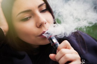 Sigarani kotini bırakın, e-suyu, e-sıvı vaping başlayın. Buharlaştırıcı cihaz kullanan güzel genç bir kadın, sigara içenler için modern bir alet. Güvenli ve lezzetli gliserin buharı