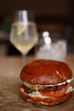 Restoran dekoratif kahverengi kağıt üzerinde büyük lezzetli burger jambon pirzola et ve taze sebze ile servis. Kafede hamburger yemek.