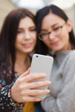 Selfie büyük gümüş mobil akıllı telefon ile alarak iki genç kız. Kameralı bir eğilimdir. Arkadaş grubu ile telefon ve paylaşım iyi fotoğraf çekmek. Aygıt üzerinde odaklanmak