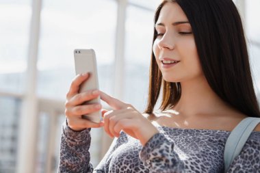 Dişlek gülümseme ile fütüristik çift kamera akıllı telefon kullanan mutlu genç beyaz kız. Şirin model, modern mobil gadget.