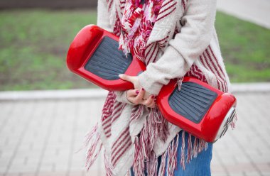 Kadın modeli modern kırmızı elektrikli mini segway ya da vurgulu kurulu scooter parkta yürürken elinde tutan. Hava kirliliği atmosfere üreten popüler yeni ulaşım teknolojisi. Kız gidişli boho tarzı kıyafetler giyiyor.