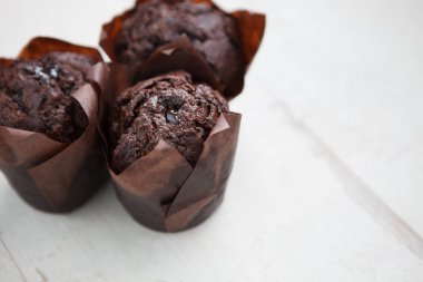 Beyaz ahşap masa üzerinde üç taze çikolatalı kek. Ev yapımı ekmek, kahve molası için almak muffin. Odak kadar yakın, metin eklemek için alanı Kopyala