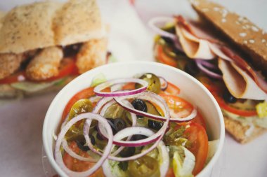 Taze sebze Yunan salatası. Kırmızı soğan halkaları, dilimlenmiş domates, biber ve siyah Nisuase zeytin. Arka plan üzerinde iki tane sandviç. Fast food restoran menüsünde Tablo.